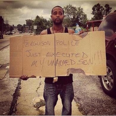 Michael Brown's stepfather holds a sign which reads, "Ferguson Police Just Executed My Unarmed Son!!!"